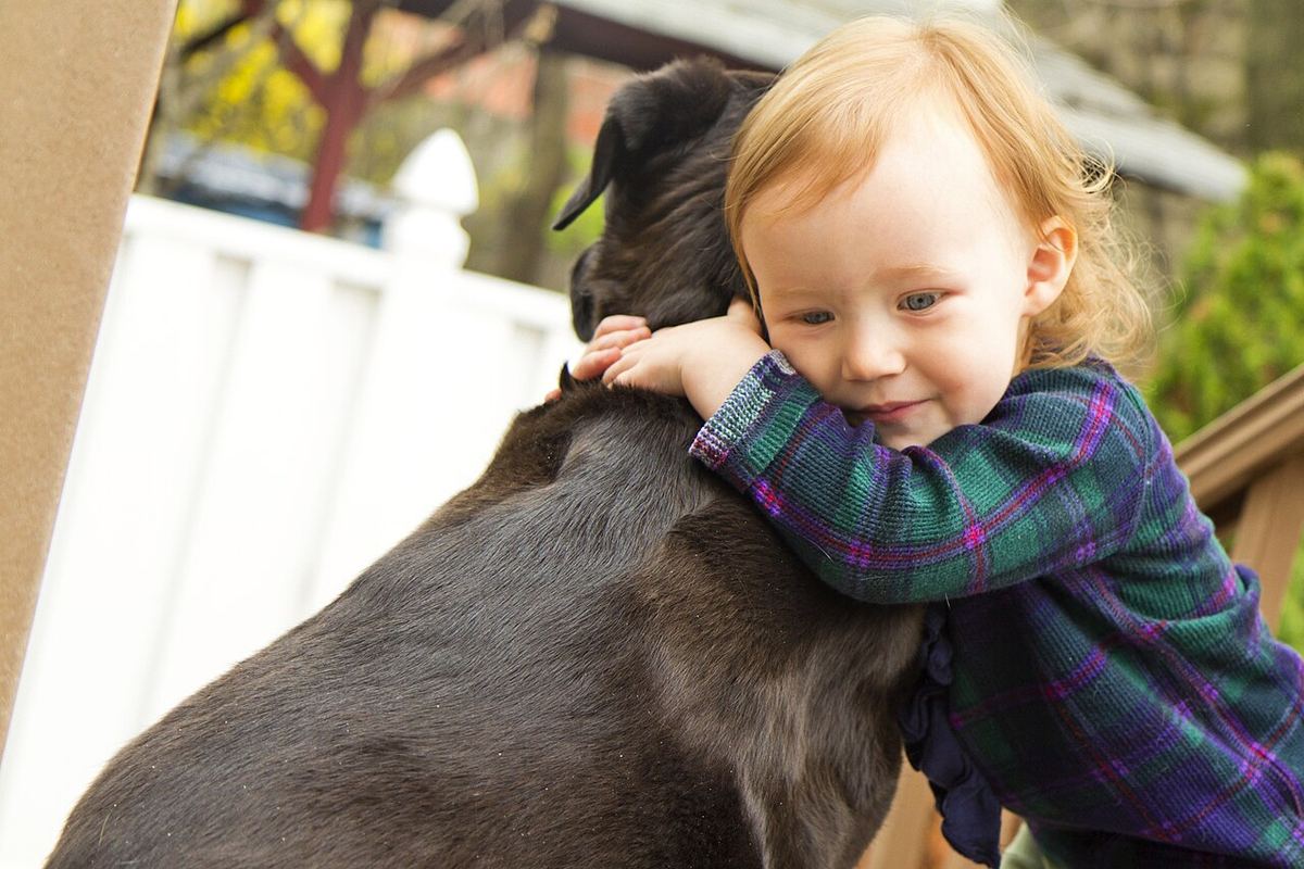 Lite barn som klemmer en hund ute i hagen